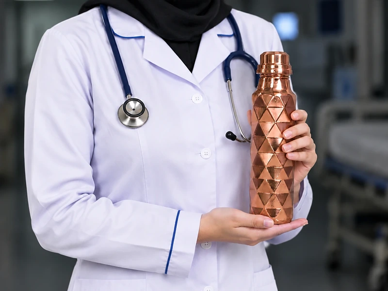پرستار با روپوش سفید و گوشی پزشکی که بطری آب مسی الماس‌تراش در دست دارد